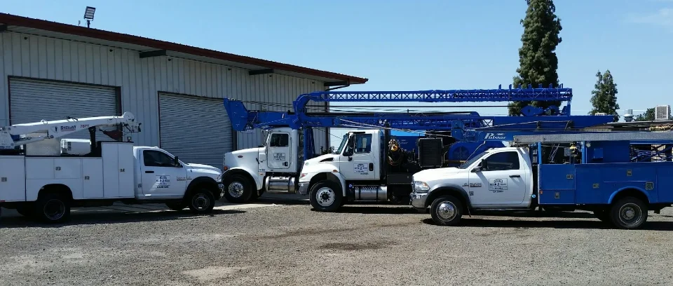 Carver Pump Service’s white service trucks and two blue pump rigs lined up on gravel in front of a metal shop building.